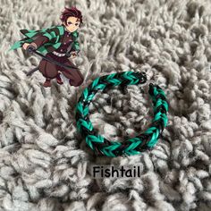 a green and black braided bracelet with an anime character on the side, next to it