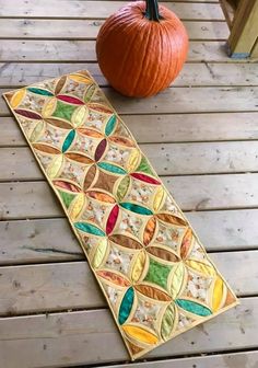 an orange pumpkin sitting on top of a wooden floor next to a quilted table runner