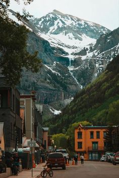 people are walking down the street in front of snow covered mountains and buildings on either side