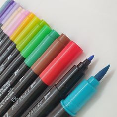 several different colored pens lined up on a white surface