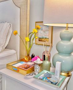 a white bed sitting next to a table with a lamp and other items on it