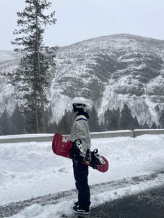 a person holding a snowboard on the side of a road with mountains in the background