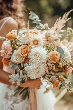 a bride holding a bouquet of white and orange flowers with greenery in the background