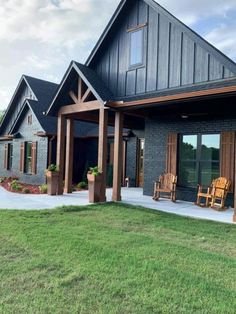 a large black house with two wooden chairs on the front porch and an attached patio