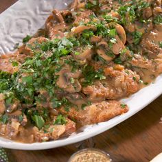 a white plate topped with meat covered in mushroom gravy and garnished with parsley