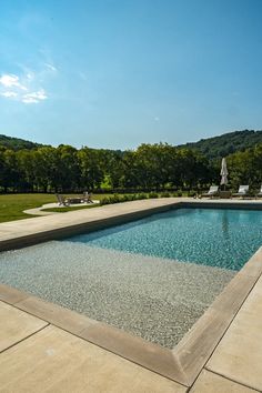 an empty swimming pool in the middle of a field with lawn chairs and trees behind it