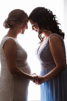 two women standing next to each other in front of a window with their hands together