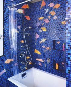 a bath tub sitting under a shower next to a blue tiled wall with fish on it