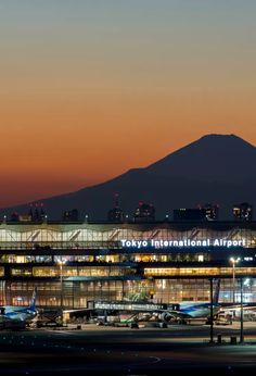 an airport at night with planes parked on the tarmac and mountains in the background