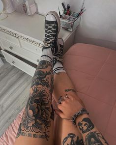 a person with tattoos on their legs sitting in front of a dresser and mirror, holding onto her leg