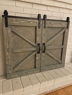 two wooden doors on the side of a white brick wall next to a wood floor