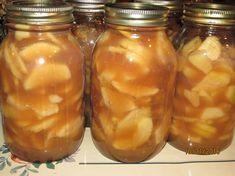 four jars filled with sliced apples on top of a table