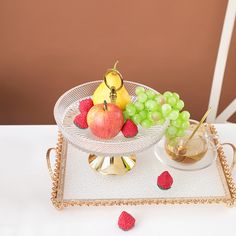 a tray with grapes, apples and strawberries on it next to a glass cup