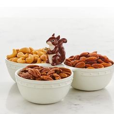 three white bowls filled with nuts on top of a marble counter next to a ceramic squirrel figurine