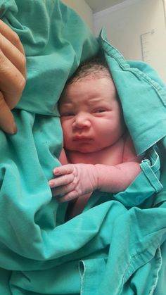 a newborn baby wrapped in a blanket is being held by someone's hand as they look at the camera