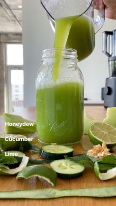 a person pouring green juice into a mason jar with cucumbers and limes