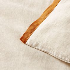 a close up of a pillow on a bed with white linen and brown leather trim