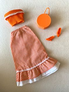 an orange and white checkered dress next to accessories for dollhouse play set on the floor