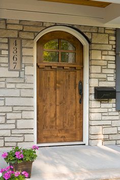 a wooden door on the side of a brick house with potted flowers in front