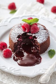 a chocolate cake with raspberries and powdered sugar on a white platter