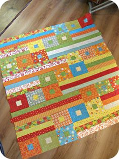 a colorful quilt is laying on the floor in front of a wooden table topper