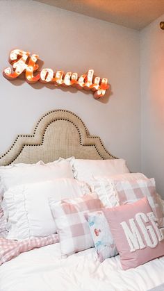 there is a bed with many pillows on it and a neon sign above the headboard