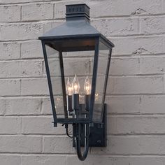 a wall mounted light with three lights on it next to a white brick wall in front of a building