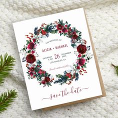 save the date card with red flowers and greenery on it, surrounded by pine branches