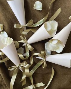 three white cones with ribbons and flowers in them on a brown cloth covered tablecloth