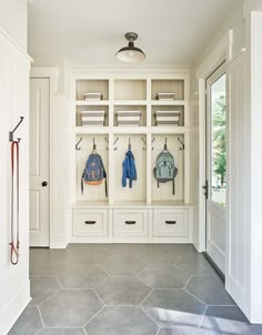 an entry way with white cabinets and gray tile flooring, two coats hanging on hooks