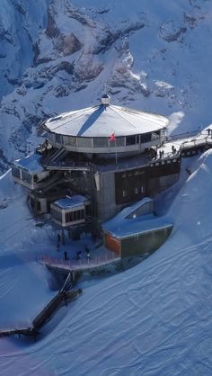 an aerial view of a building on top of a snowy hill with mountains in the background