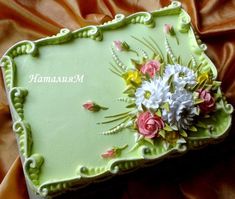 a green cake with flowers on it sitting on top of a bed covered in orange sheets