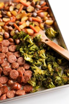 sausage and broccoli on a baking sheet with a wooden spatula in it