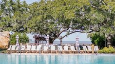 an empty swimming pool surrounded by trees with chairs and tables on the edge in front of it