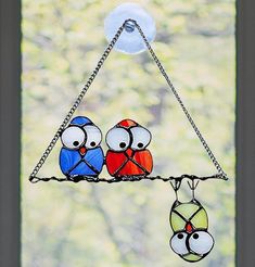 three colorful birds sitting on a chain hanging from a window