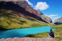 a man sitting on top of a rock next to a blue lake in the mountains