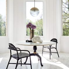 a dining room table with chairs and a vase on it in front of two windows