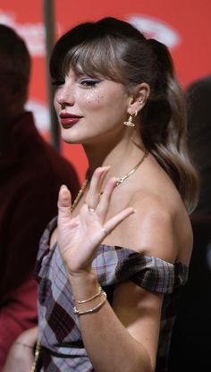 a woman with her hand up in the air while wearing gold jewelry and red lipstick