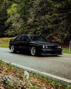 a black car is driving down the road in front of some trees and grass,