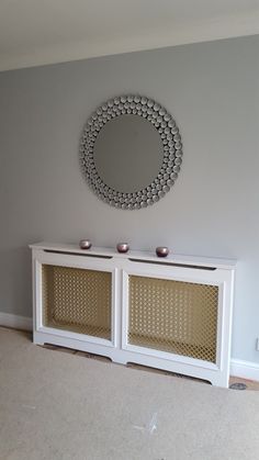 a white entertainment center with wicker doors and a round mirror on the wall