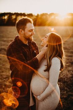 a pregnant woman and man standing in an open field with the sun shining down on them