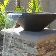 a water fountain is shown in front of a building with plants and trees around it