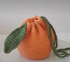 an orange crocheted bag with a green leaf on the front and side, sitting on a white surface