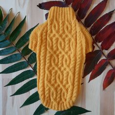 a yellow knitted mitt sitting on top of a wooden table next to leaves