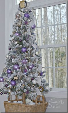 a white christmas tree with purple and silver ornaments in a wicker basket next to a window