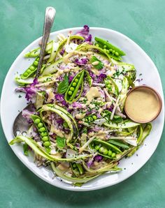 a white plate topped with green vegetables covered in dressing next to a fork and spoon