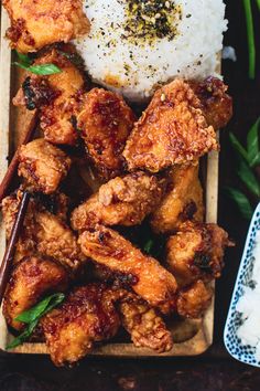 chicken wings with rice and herbs on a wooden tray next to other food items, including chopsticks