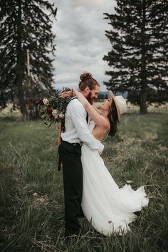 a bride and groom are kissing in the grass by some trees at their wedding day