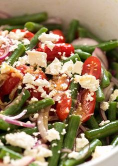 a white bowl filled with green beans, tomatoes and feta cheese on top of it