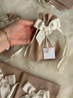 a woman's hand is holding two small gift bags with bows on them and tags attached to them